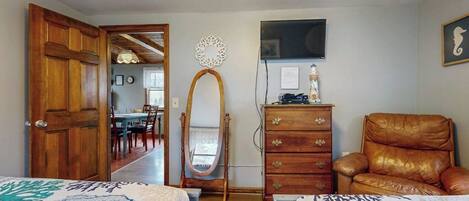 A room with two beds, a wooden dresser, a leather chair, a mirror, and a television on the wall.