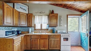 A kitchen with wooden cabinets, a microwave, a stove, and a sink. - Cozy Cottage with Private Deck - Walk to Short Sands Beach (York)