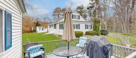 A deck with outdoor furniture, a grill, and a view of a house and yard.