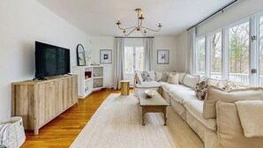 Sala de estar com sofá, televisão, armário de madeira e janelas amplas.