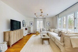 A living room with a sofa, television, wooden cabinet, and large windows.