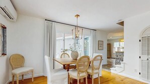Uma sala de jantar com uma mesa de madeira, quatro cadeiras, um candelabro e vista através de grandes janelas.