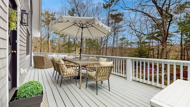 Um terraço com mesa, cadeiras, guarda-sol e corrimão branco.