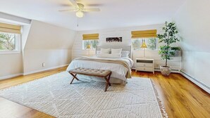 Quarto com cama, mesas de cabeceira, ventoinha no teto, janela e um vaso com planta.