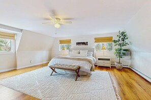 A bedroom with a bed, bedside tables, a ceiling fan, a window, and a potted plant.