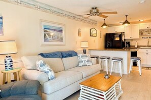 Ein Wohnzimmer mit einer Couch, einem Couchtisch und einer Küchenzeile mit Kühlschrank und Barhockern.