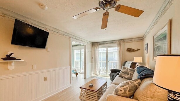 A living room with a ceiling fan, a television, a sofa, a coffee table, and a lamp. - Coastal luxury condo steps from Wells Beach w/ AC, WiFi & full kitchen (Wells)