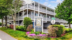 A multi-story building with balconies, a signboard with contact information, and a landscaped garden with flowers. - Coastal luxury condo steps from Wells Beach w/ AC, WiFi & full kitchen (Wells)