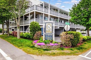 Ein mehrstöckiges Gebäude mit Balkonen, einer Schilder mit Kontaktinformationen und einem angelegten Garten mit Blumen.