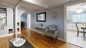 Ampla sala de estar com piso de madeira, mesa de jantar, poltrona estampada e console branco com um vaso.