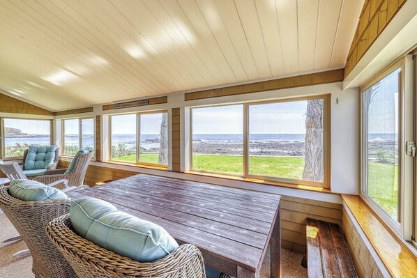 A covered outdoor seating area with a wooden table and wicker chairs, large windows with a view of the landscape. - Beautiful waterfront house & cottage w/ a firepit - walk to the beaches & town (York)
