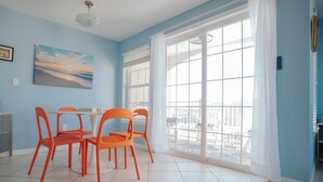 Ein Essbereich mit einem Tisch, vier orangen Stühlen, einem Bild an der Wand und einem großen Fenster mit Vorhängen.