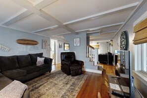 Ein Wohnzimmer mit einem dunkelgrauen Sofa, einem Ledersessel, einem gemusterten Teppich und einem Fernseher auf einem Lowboard.