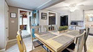 A dining area with a long table, chairs, a ceiling fan, and a kitchen in the background. - Gorgeous dual-unit, perfect for large groups Dogs are welcome (York)