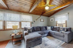 Ein gemütliches Wohnzimmer mit einer Eckcouch, Holzbalken an der Decke und einem Deckenventilator.