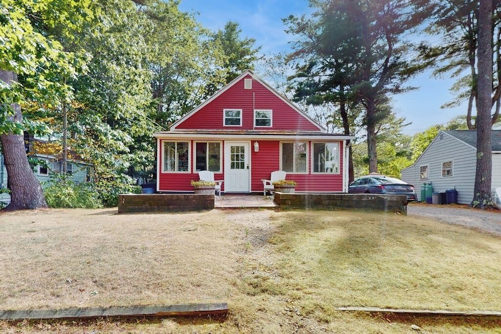 A red single-story house with a front porch, a small attached garage, and a well-maintained lawn.