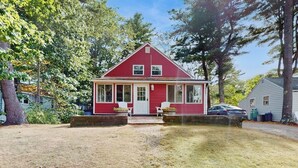 Ein rotes Einfamilienhaus mit Veranda, kleinem Anbau für eine Garage und einem gepflegten Rasen.