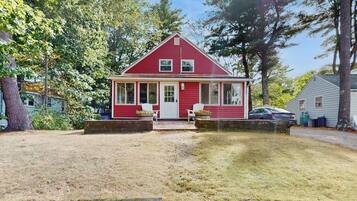 A red single-story house with a front porch, a small attached garage, and a well-maintained lawn.