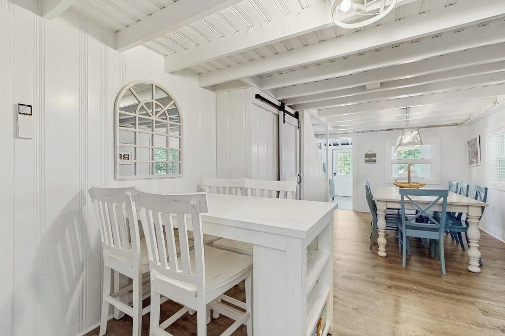 A dining area with a white table and chairs, a large arched window, and a ceiling with exposed beams.