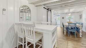 Ein Essbereich mit einem weißen Tisch und Stühlen, einem großen Bogenfenster und einer Decke mit freiliegenden Balken.
