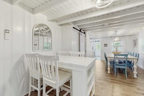 A dining area with a white table and chairs, a large arched window, and a ceiling with exposed beams. - Charming York cottage close to beach with firepit & sunroom - dogs welcome (York)