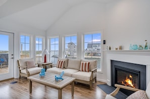 A spacious living room with a sofa, chairs, a coffee table, a fireplace, and large windows overlooking a body of water.