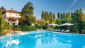 Ein Pool mit Liegestühlen und Sonnenschirmen, umgeben von Grünpflanzen und einem Gebäude.