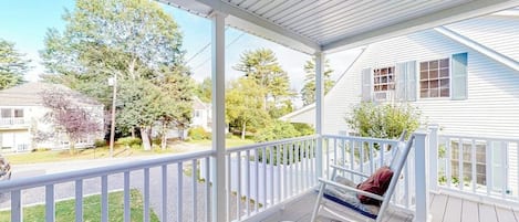 Une véranda couverte avec une balustrade blanche, une chaise berçante et une table.