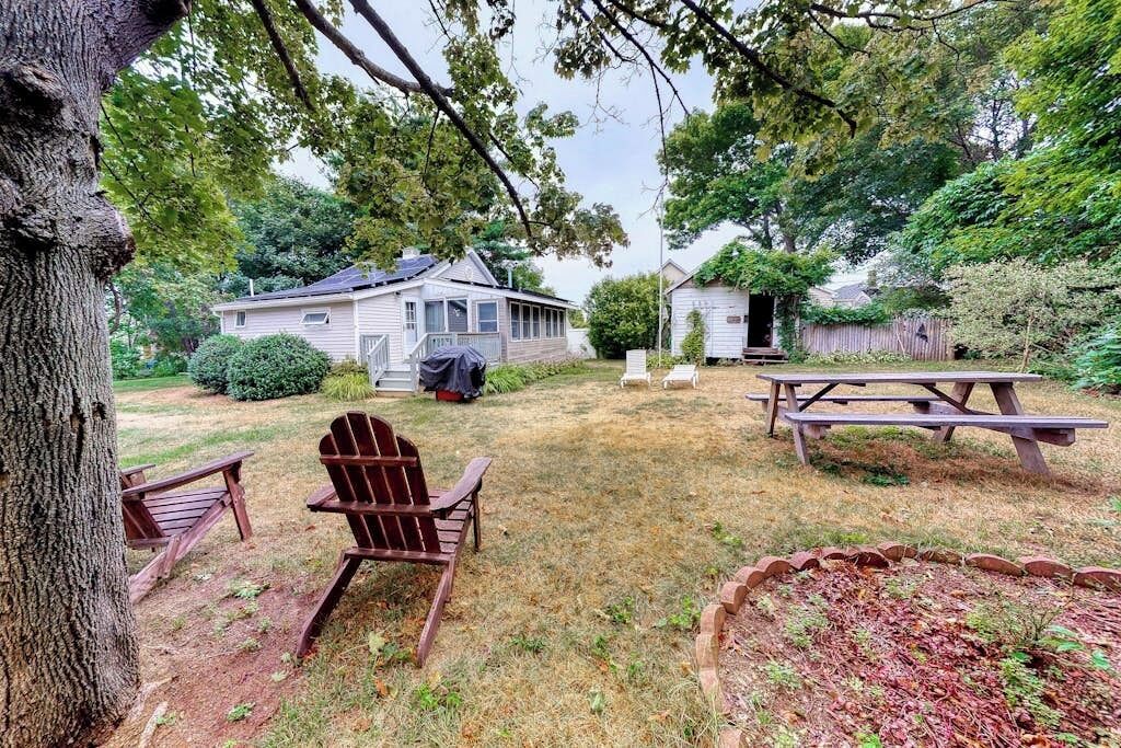 A backyard with a wooden deck, a picnic table, and two Adirondack chairs.