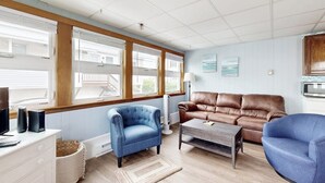 Una sala de estar con un sofá de cuero marrón, un sillón azul, un tocador blanco y un televisor.