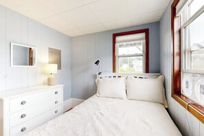 Un dormitorio con cama, cómoda, espejo, lámpara y ventana.