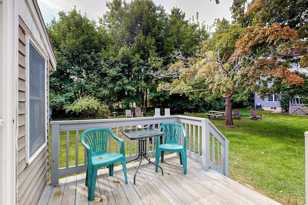 A wooden deck with a table and chairs, surrounded by a white railing, and a grassy yard with trees.