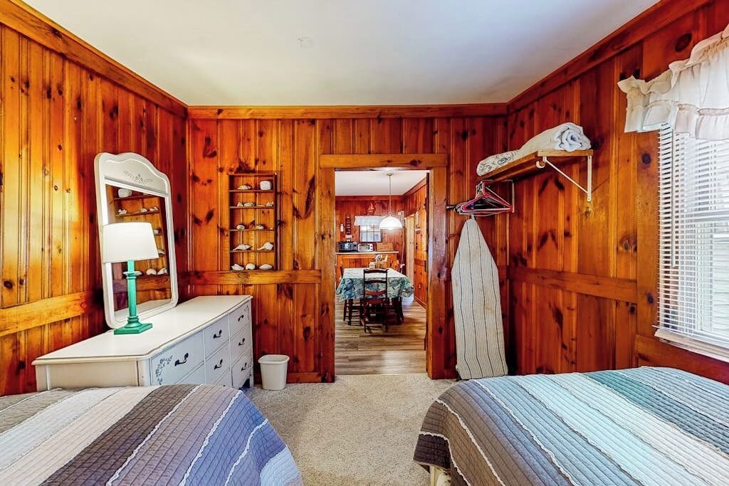 A wooden-paneled room with a dresser, mirror, and two beds.