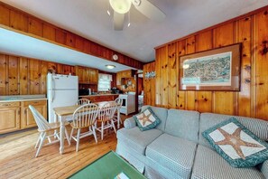A cabin with wooden walls, a dining area with a table and chairs, a kitchenette, and a living area with a sofa.
