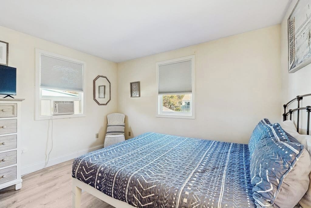 A bedroom with a bed, dresser, chair, and two windows.