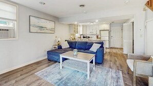 Ein Wohnzimmer mit einem blauen Sofa, einem Couchtisch und einer Küche im Hintergrund.