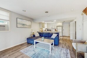 A living room with a blue sofa, a coffee table, and a kitchen in the background.