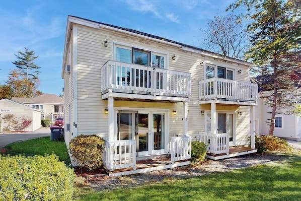 A two-story residential building with a balcony on the second floor, a front porch, and a garage.