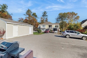 A residential street with houses, a barbecue grill, and parked cars.