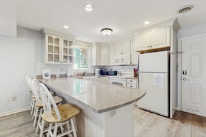 A kitchen with white cabinets, a granite island, and a refrigerator.