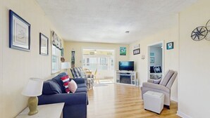 A living room with a sofa, armchair, TV, and a small table with a lamp.