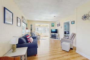 A living room with a sofa, armchair, TV, and a small table with a lamp.