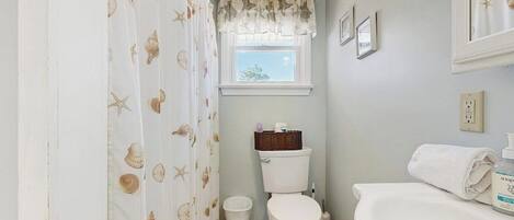 A bathroom with a toilet, a sink, a window with a view, and a shower curtain with a sea shell pattern.