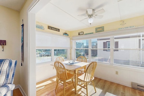 A dining area with a table and chairs, a ceiling fan, and a view through large windows.