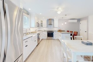 Eine moderne Küche mit weißen Schränken, einem Edelstahlkühlschrank, einem eingebauten Backofen und einem Essbereich mit weißen Stühlen.