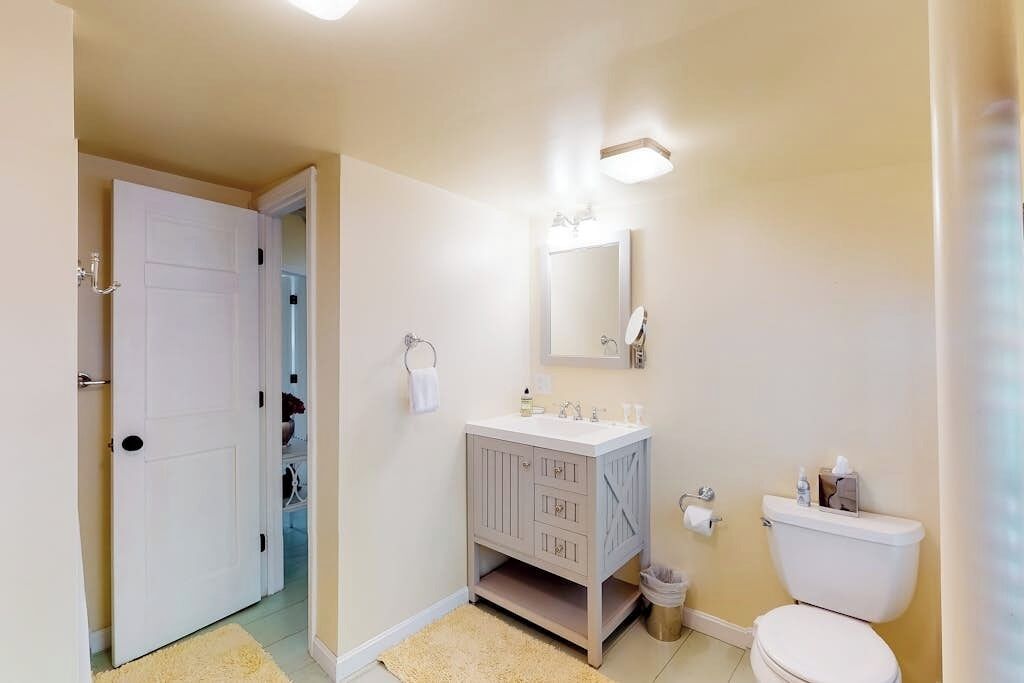 A bathroom with a toilet, sink, mirror, and a door leading to a hallway.
