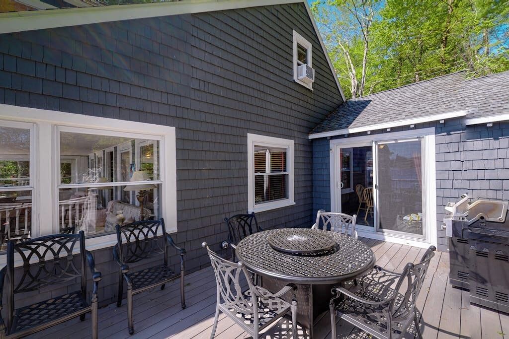 A deck with a round table and chairs, a grill, and a sliding glass door.