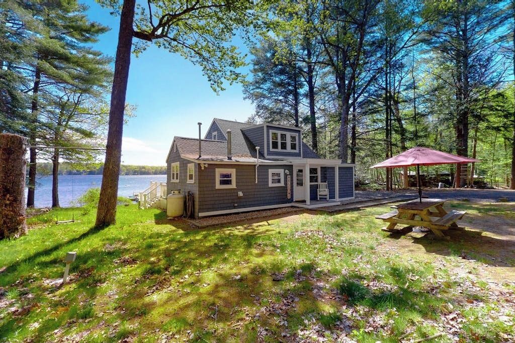 Une cabane avec une terrasse, une table de pique-nique et une vue sur un lac.