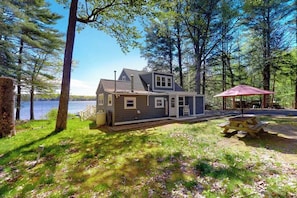 A cabin with a deck, a picnic table, and a view of a lake. - Charming lakefront cottage with a dock, WiFi, & washer/dryer - dogs welcome (Windham)