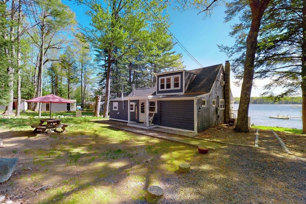 A cabin with a porch, a picnic table, and a view of a lake.